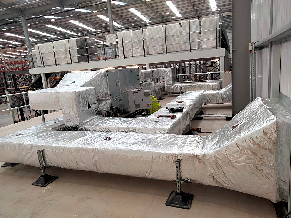 Insulated rectangular ductwork run off the air handling unit, carried on plinths and set level the length of the building. GS Yuasa, Swindon.